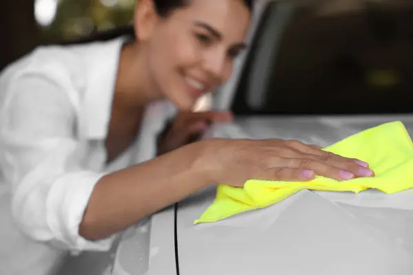 Woman cleaning car hood with rag outdoors, selective focus