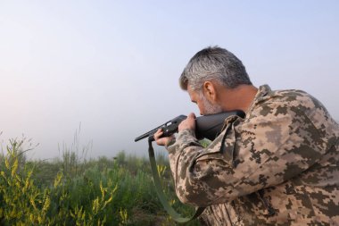 Kamuflaj giyen ve av tüfeğini dışarıya doğrultmuş bir adam. Metin için boşluk