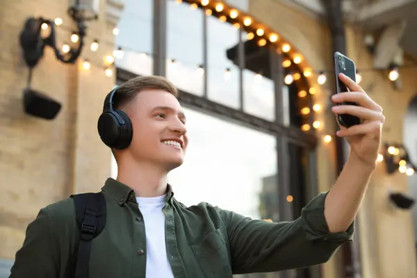 Smiling man in headphones taking selfie outdoors, low angle view