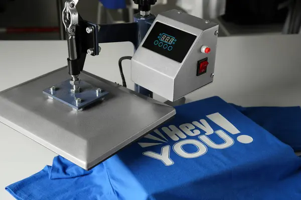 Printing logo. Heat press with blue t-shirt on white table, closeup