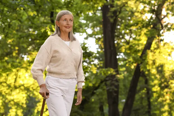 Senior woman with walking cane in park. Space for text