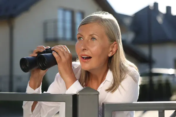 stock image Concept of private life. Curious senior woman with binoculars spying on neighbours over fence outdoors