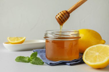 Dipper 'dan kavanoza tatlı bal damlıyor ve beyaz masada taze limonlar, mesaj için yer var.