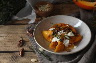 Peynir, kekik ve cevizle servis edilen fırınlanmış balkabağı dilimleri ahşap masada, mesaj için yer var.