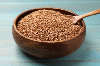 Açık mavi ahşap masada kuru karabuğdaylı kase ve kaşık, yakın plan.