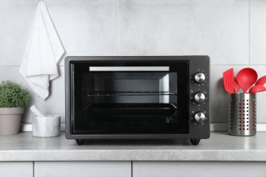 Kapalı alandaki gri masada elektrikli fırın ve mutfak aletleri.