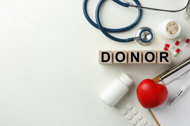 Tahta küplerde kelime donörü, küçük kırmızı kalp ve beyaz masa üzerinde haplar, düz yatak. Metin için boşluk