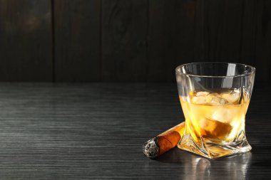 Bir bardak buzlu viski ve siyah ahşap masada yanan puro. Metin için boşluk
