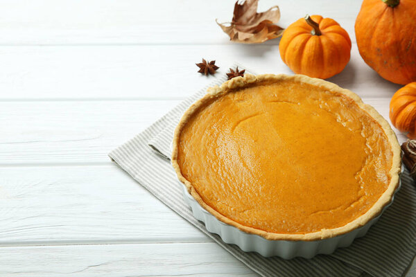 Delicious pumpkin pie and ingredients on white wooden table. Space for text