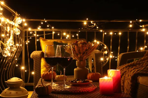 Glasses of wine, burning candles and decor on rattan table. Autumn evening on terrace