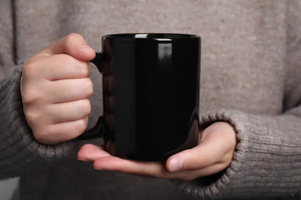 Woman holding black mug of drink, closeup