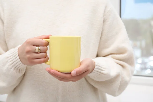 Woman holding yellow mug indoors, closeup. Mockup for design