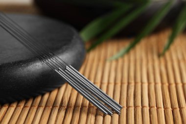 Bambu hasırının üzerinde akupunktur iğneleri ve spa taşı, yakın plan.