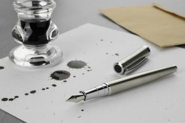 Şık dolmakalem, mürekkep lekeli kağıt ve açık gri masa üzerinde mürekkep.