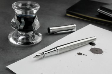 Şık dolmakalem, mürekkep lekeli kağıt ve gri desenli masa üzerine mürekkep.
