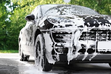 Auto covered with cleaning foam at outdoor car wash clipart