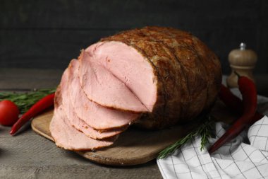 Lezzetli fırınlanmış jambon, domates, acı biber ve biberiye gri ahşap masada.