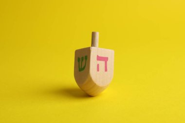 Wooden dreidel on yellow background. Traditional Hanukkah game clipart