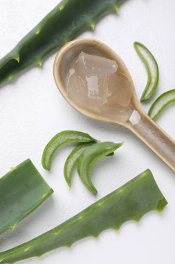 Beyaz arka planda kaşık ve bitki dilimleri içinde Aloe vera jeli, düz yatıyordu