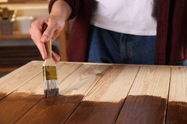 Fırçalı bir adam ahşap zemine ahşap leke sürüyor. Kapalı alanda, yakın plan.