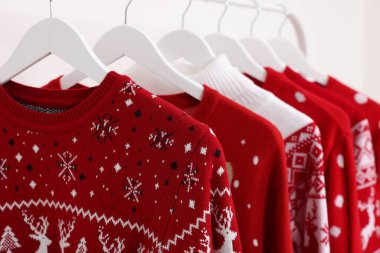 Beyaz arka planda farklı Noel süveterleri olan raflar, yakın plan.