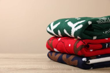 Ahşap masada bej arka planda duran farklı Noel süveterleri yığını, yakın plan. Metin için boşluk