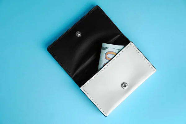 Open leather purse with money on light blue background, top view