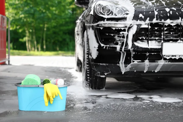 Car cleaning supplies and auto covered with foam outdoors