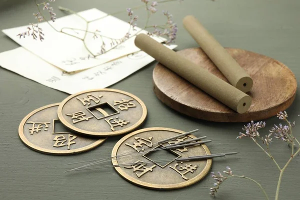 Acupuncture needles, moxa sticks and antique Chinese coins on grey wooden table, closeup