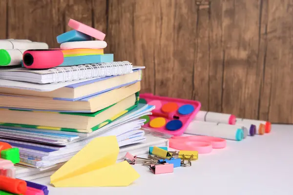 Many different books, paper plane and school stationery on white table, space for text. Back to school
