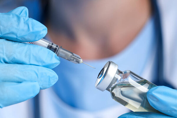 Doctor inserting syringe into glass vial with medication, closeup