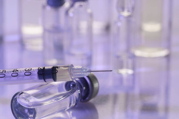 Glass vial and syringe with medication on white table, closeup. Space for text