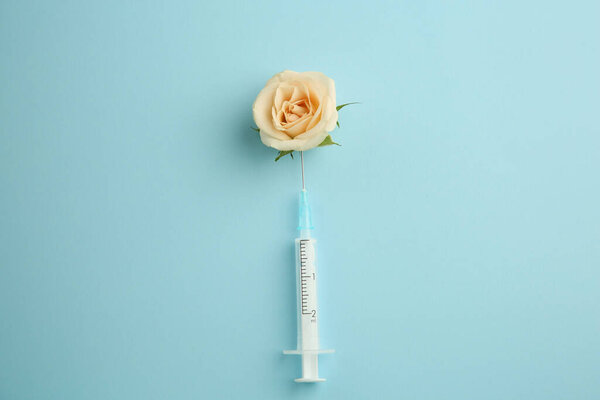 Medical syringe and beautiful rose on light blue background, top view