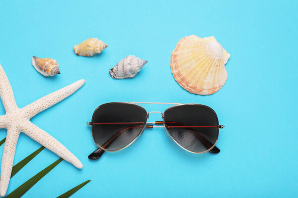 Stylish sunglasses, starfish and seashells on light blue background, flat lay