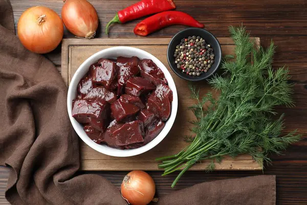 Çiğ sığır ciğerini soğan, baharat, kırmızı biber ve ahşap masada dereotla kes.