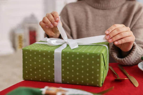Woman opening gift box at table indoors, selective focus