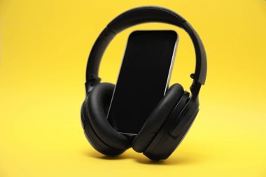 Sarı arka planda modern kablosuz kulaklık ve akıllı telefon.
