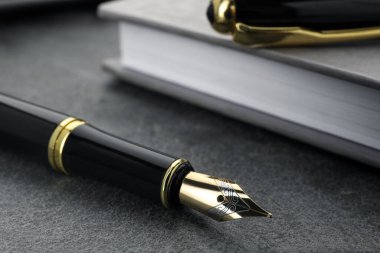 Gri desenli masa üzerinde siyah dolmakalem ve defter, yakın plan.