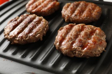 Lezzetli hamburger köfteleri elektrikli ızgarada pişiyor, yakın plan.