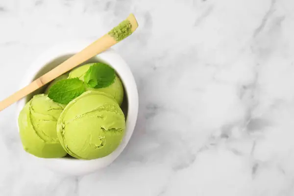 Tasty matcha ice cream in bowl and spoon with powder on white marble table, top view. Space for text