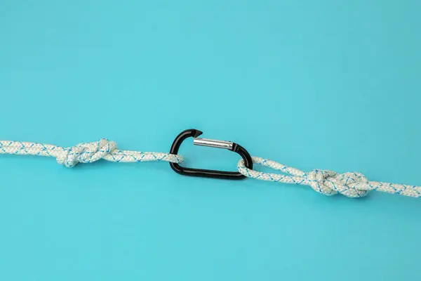 One metal carabiner with ropes on light blue background