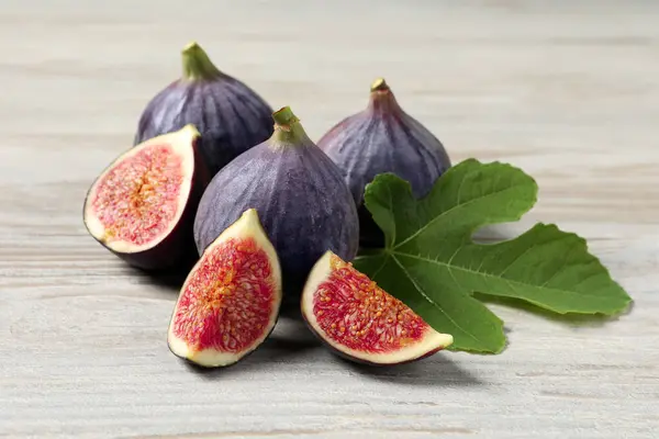 Whole and cut ripe figs with leaf on light wooden table, closeup