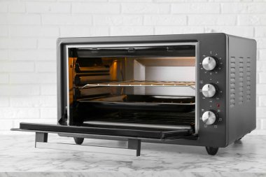 Tuğla duvarın yanındaki beyaz mermer masada bir elektrikli fırın.