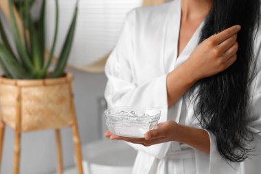 Kapalı mekanda bir kase aloe saç maskesi tutan genç bir kadın, yakın plan. Metin için boşluk