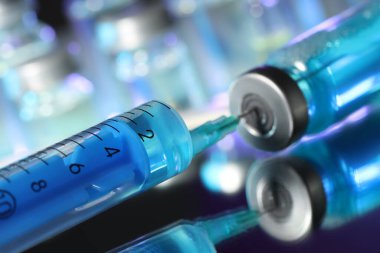 Şırıngayı ayna yüzeyindeki ilaç şişesiyle dolduruyorum.