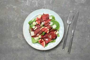 Gri desenli masada servis edilen leziz bresaola salatasıyla servis edilen tabak düz.