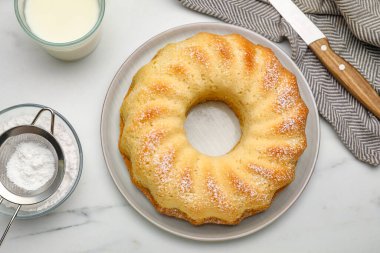 Pudra şekerli lezzetli sünger keki, beyaz masada bir bardak süt ve bıçak, düz uzanmış.