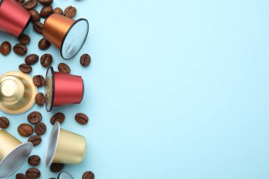 Açık mavi arka planda bir sürü kahve kapsülü ve fasulye, düz bir zemin. Metin için boşluk