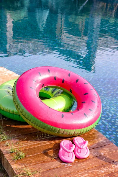 Inflatable rings and flip flops on wooden deck near swimming pool. Luxury resort