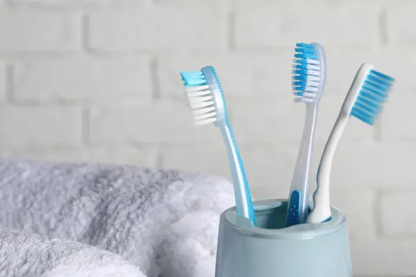 Plastic toothbrushes in holder and towels near white brick wall, closeup